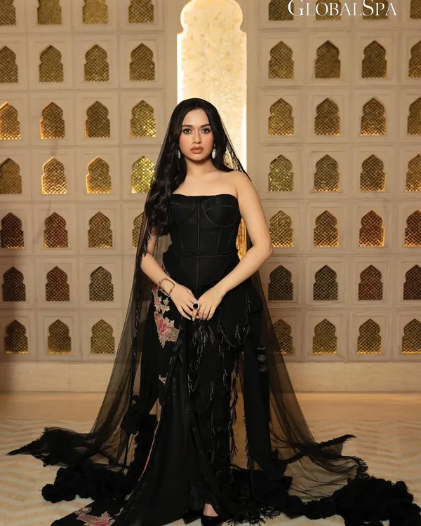 A full-length editorial shot of actress Jannat Zubair for GlobalSpa Magazine. The image is set against an ornate, traditional backdrop, contrasting with her modern black couture gown to create a visually rich portrait.
