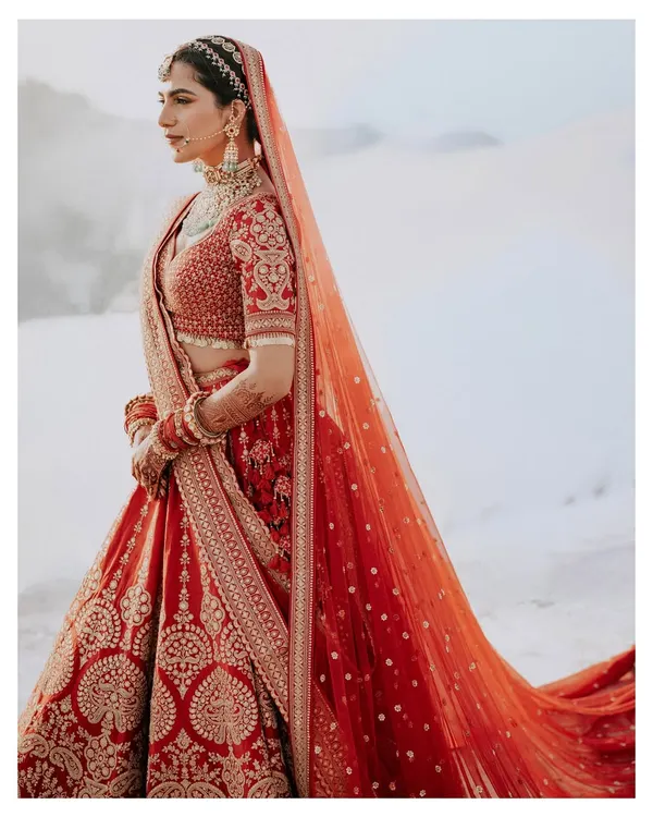 A powerful and elegant bridal portrait. The bride's striking red lehenga stands out against the stark white background, creating a high-fashion, editorial look.
