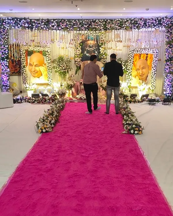 A wide view of a large-scale satsang event I decorated. The grand stage is the focal point, and I used a vibrant pink ruffled carpet for the walkway to create a welcoming path for devotees.