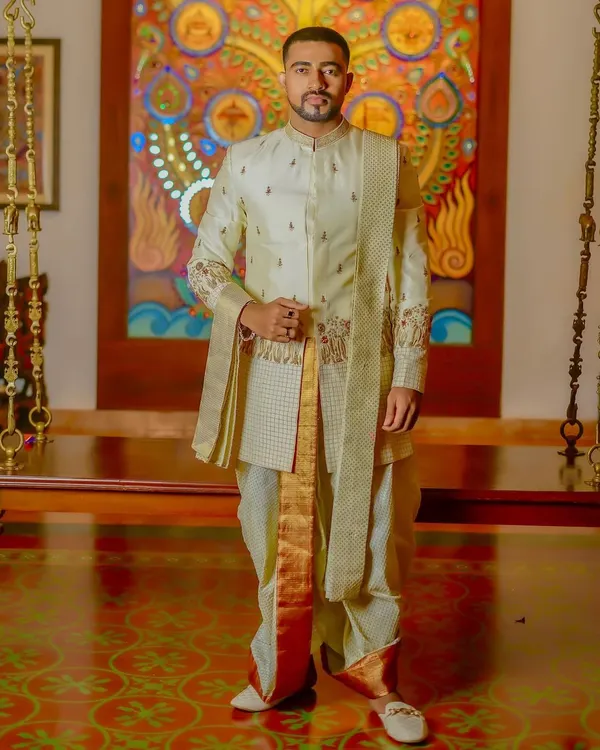This is a complete look I designed for a South Indian groom. It features a layered, embroidered sherwani in a subtle off-white, paired with a traditional silk dhoti and shawl (angavastram) for a regal and authentic appearance.