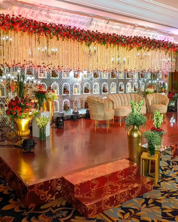 This reception stage is a floral fantasy. I created a massive backdrop wall with intricate white jaali niches holding candles, topped with a dense ceiling of hanging white and red flowers for a truly opulent and royal look at The Leela.