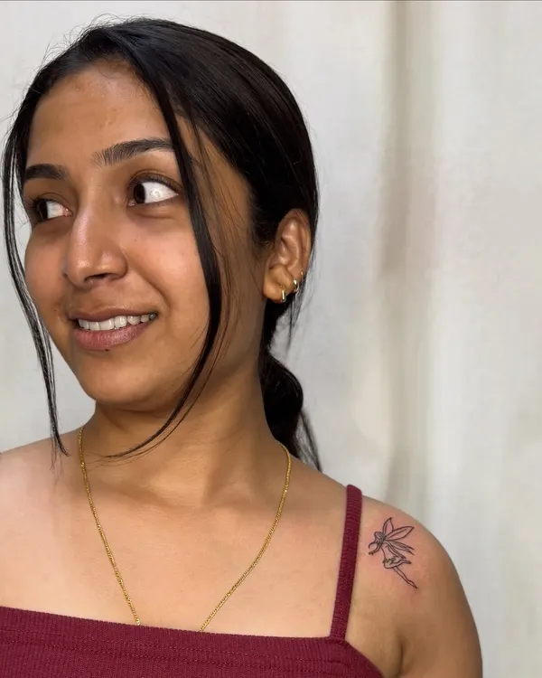 A delicate fine-line fairy tattoo on the shoulder. This minimalist piece captures a sense of magic and whimsy with just a few simple, elegant lines.