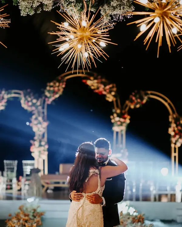 A magical first dance under a sky of starburst chandeliers. The combination of warm lighting, floral arches, and a touch of haze creates a truly cinematic and romantic reception moment.