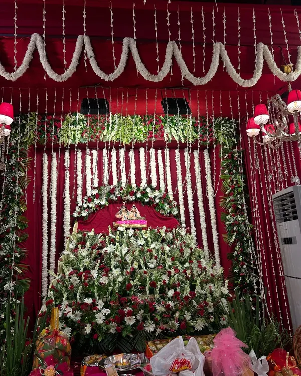 A full view of our Radha Ashtami decor, featuring a grand floral stage for the deity. We used a combination of red, white, and green flowers against a rich maroon fabric backdrop to create a traditional and opulent look.