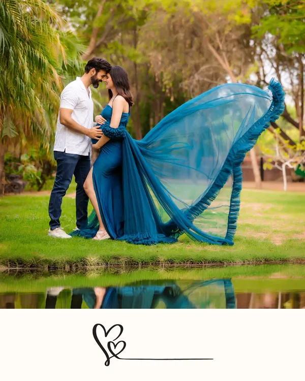 A breathtaking outdoor shot by the water, with the reflection adding a magical quality. The wind catches the mother-to-be's blue gown, creating a moment of pure drama and beauty.