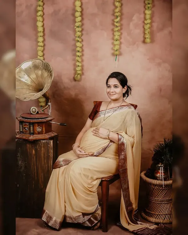 A full portrait of the mother-to-be, seated gracefully in our traditional setup. The warm lighting and classic props like the gramophone highlight the beauty of this special time.