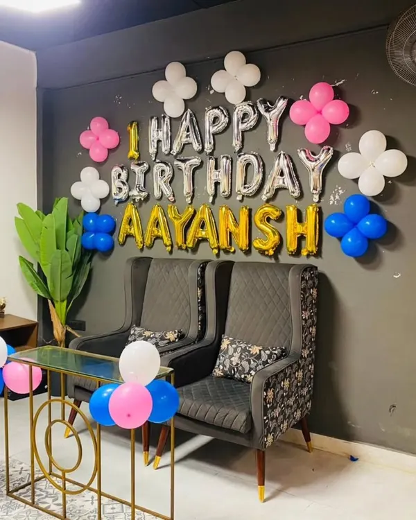 A simple and elegant wall decoration for a first birthday at home. This setup uses foil balloons to spell out "Happy Birthday Aayansh" and is accented with small balloon clusters for a clean and modern look.