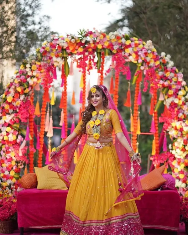 Here is a perfect example of a vibrant Haldi backdrop. I created a full floral arch with a mix of colorful flowers and hanging tassels to frame the bride beautifully, making her the radiant center of attention.