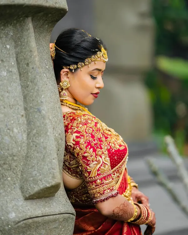 A moment of quiet reflection for the bride. Her custom red and gold saree, with its heavily embroidered blouse featuring peacock motifs, was designed to be a timeless piece of her wedding story.