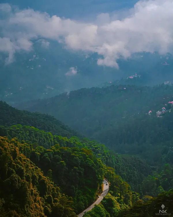 The serpentine roads of the Himalayas. This shot captures the moody, atmospheric conditions of a monsoon drive, with low-hanging clouds blanketing the lush green hills.