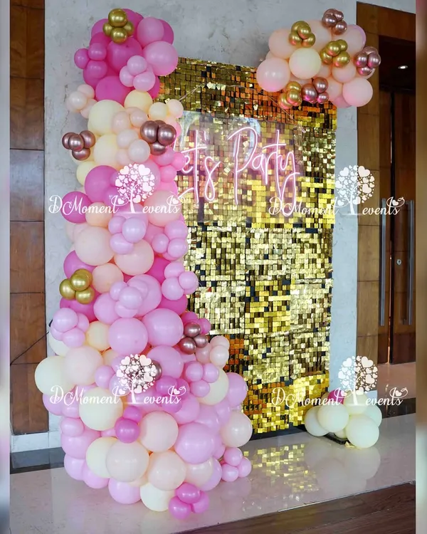 We created this glamorous photo corner for a boho-themed Annaprashan ceremony. It features a shimmering gold sequin wall, a custom "Let's Party" neon sign, and an organic arrangement of pink, white, and chrome gold balloons for a fun and modern look.