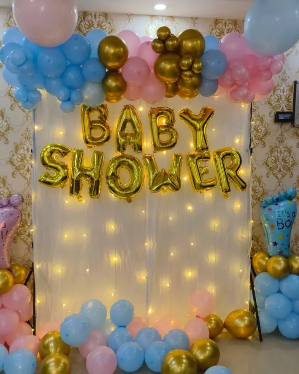A classic gender reveal baby shower backdrop. This setup includes a fairy light curtain, "BABY SHOWER" foil balloons, and balloon pillars with "It's a Girl" and "It's a Boy" foils, keeping the surprise.