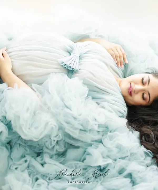 A moment of pure serenity. This overhead shot captures the mother-to-be enveloped in a cloud of soft blue tulle, creating a dreamy and peaceful fine art portrait.