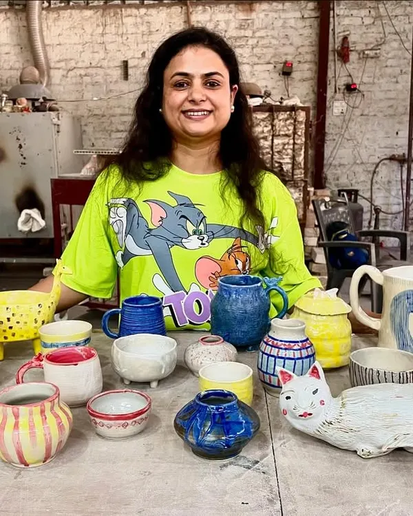 The wonderful result of a beginner's workshop. This student is proudly showing her first collection of handmade ceramic pieces, including mugs, bowls, and a very creative cat planter.