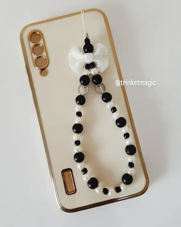 Add a little balance to your bling with this black and white beaded phone strap. It features a cute bow and is attached to a phone, showing how it can elevate your tech.