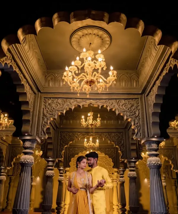 A couple stands in a majestic hall with golden lighting and intricate architecture. This shot is perfect for a royal-themed pre-wedding shoot.