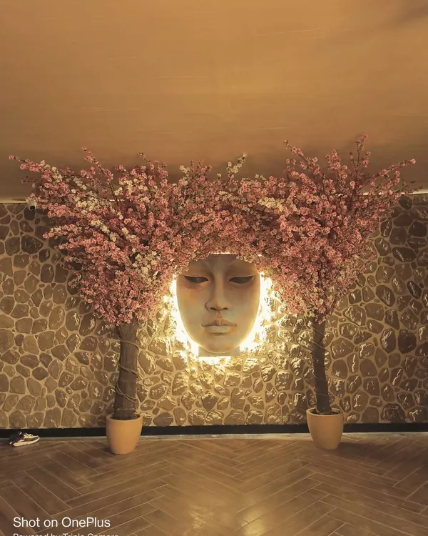A dramatic installation featuring two large artificial pink cherry blossom trees framing a backlit sculpture. This creates a serene and artistic focal point in this hospitality space.