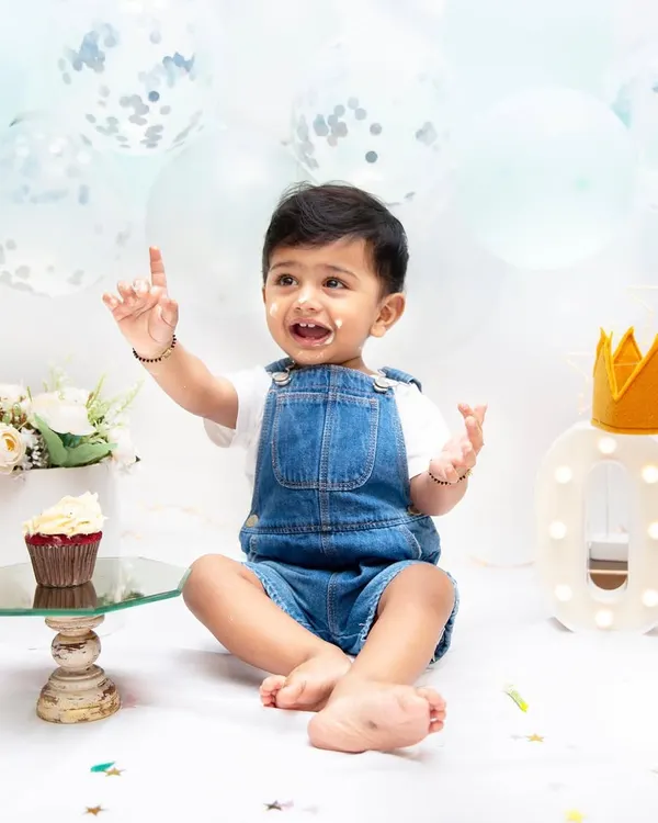 A first birthday cake smash is a momentous occasion. This little one, pointing up with a bit of cake on his face, is a perfect picture of curiosity and delight.