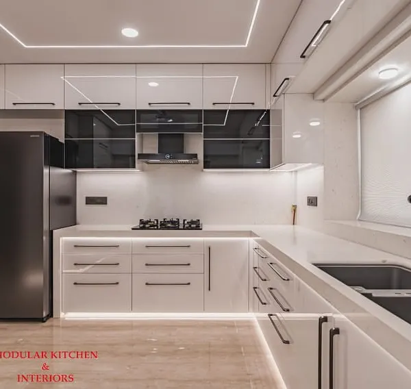 A stunning white modular kitchen in Mumbai Central, featuring an anti-scratch acrylic mirror finish and accents of grey-tinted glass. The high-gloss surface reflects light beautifully, making the space feel large and luxurious.