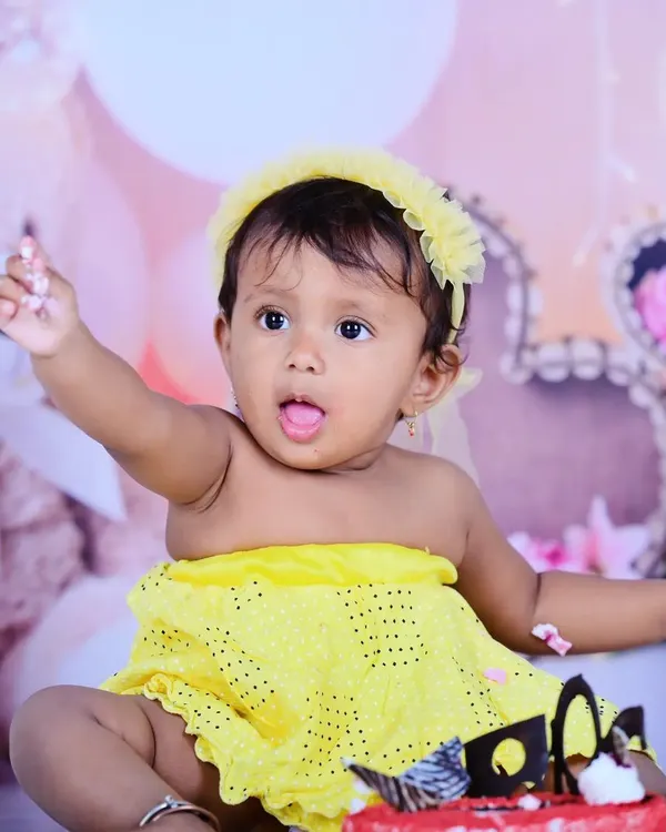 A sweet first birthday shot with a cake, where the little girl is dressed in a bright yellow outfit.