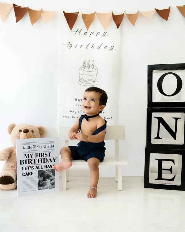 A perfect first birthday portrait. This little boy looks absolutely dapper in his bow tie and suspenders, sitting happily in a clean, modern setup with a teddy bear and "ONE" blocks.