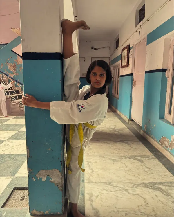 A young student with a yellow belt demonstrates an impressive standing wall split, showing amazing flexibility and control.