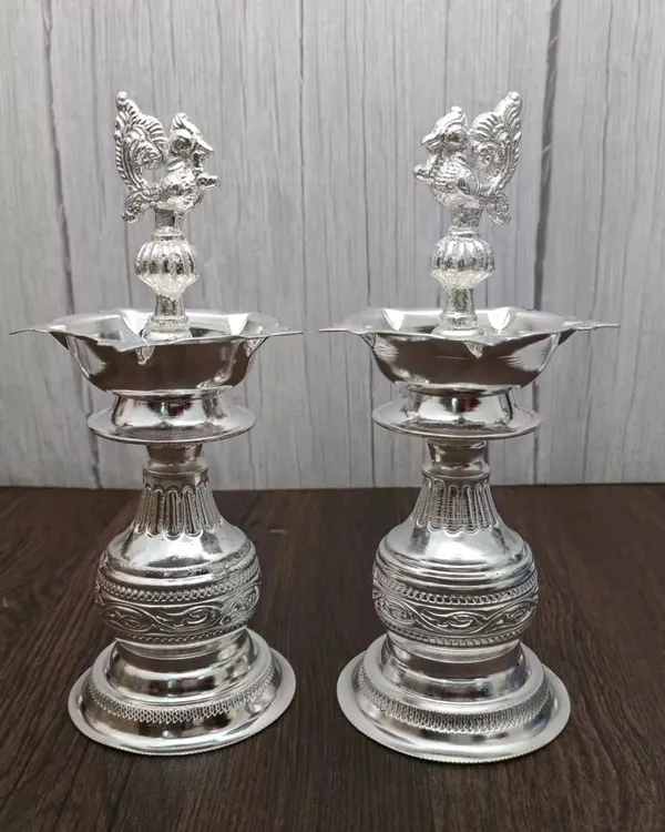 This pair of German silver Nakashi deepams stands tall and elegant. The intricate carving on the base and the peacock design on top make these standing lamps a stunning addition to any pooja room or doorway.