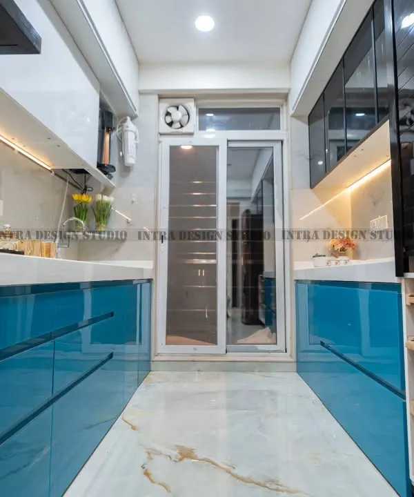 A full view of a vibrant blue parallel modular kitchen we designed in Ulwe. The glossy blue acrylic finish on the lower cabinets contrasts beautifully with the white overhead units and marble-patterned flooring, creating a long, seamless, and modern look.