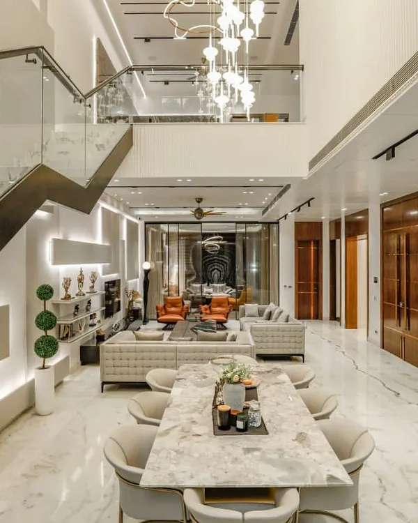 An expansive view of the H-360 Vikaspuri residence, showing the integration of the dining area and the double-height living space. The floating staircase and glass railings maintain an open, airy feel, connecting the different levels of the home.