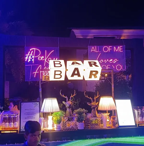 A full view of our glamorous bar setup for a sangeet night, complete with custom neon signs like '#PeeKeTalli' and romantic quotes. This shows how we can transform a space and create a high-energy focal point for your celebration.