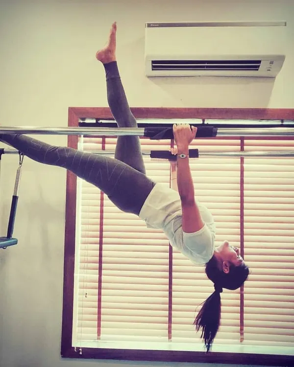 Hanging exercises on the Cadillac are excellent for spinal decompression and building serious core and upper body strength. This pose requires a high level of control and flexibility.