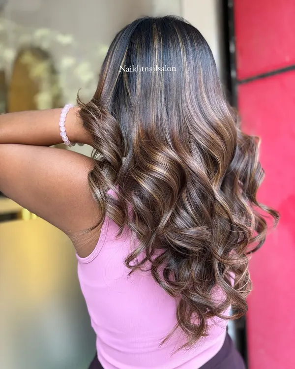 This side view highlights the placement of lighter balayage pieces that frame the face and add brightness. The blend of warm and cool brown tones creates a sophisticated look on these expertly styled curls.