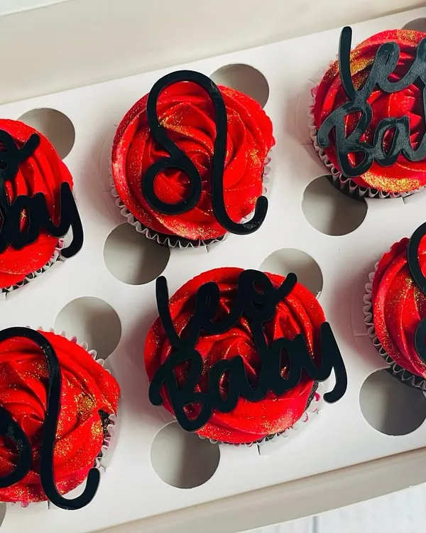 Celebrate a Leo's birthday with this bold and beautiful cupcake set. The rich chocolate cupcakes are topped with vibrant red buttercream, a sprinkle of gold glitter, and custom black acrylic toppers featuring the Leo zodiac symbol.