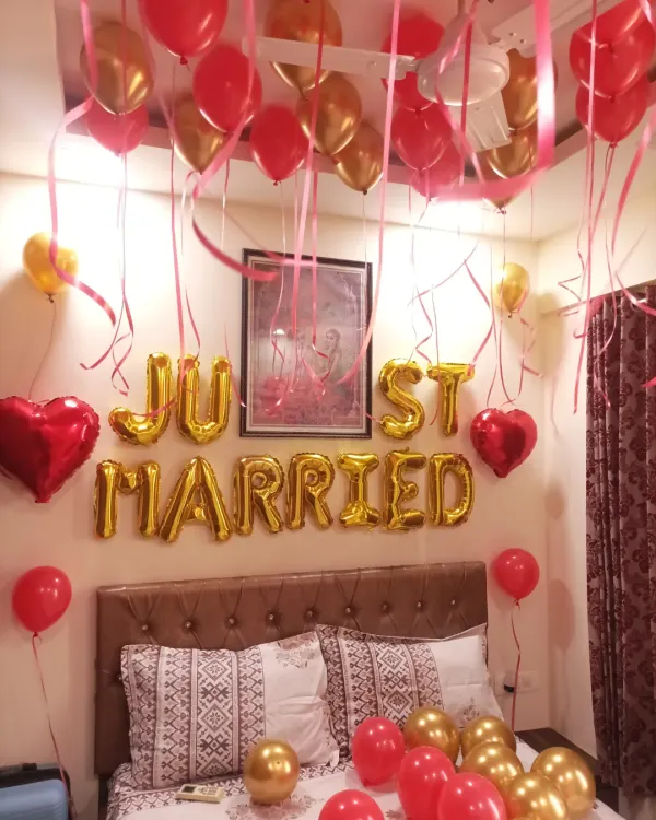 A classic 'Just Married' room decoration. The setup includes gold foil letter balloons over the bed, with red and gold balloons on the floor and ceiling.