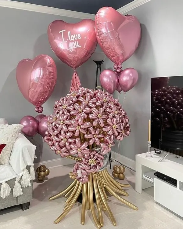 A truly unique gift: a giant flower bouquet made entirely of balloons. This stunning pink and gold creation is surrounded by heart-shaped foil balloons for a romantic gesture.