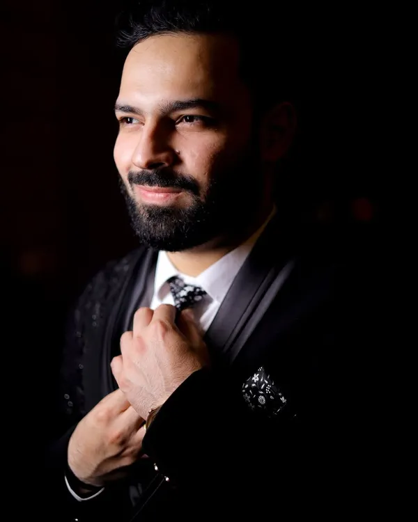 A classic, moody portrait of the groom adjusting his tie. The dramatic lighting creates a sophisticated and timeless look.