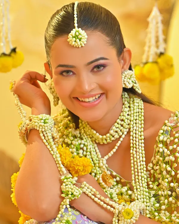 A radiant Haldi look. The makeup for this ceremony is all about a fresh, natural glow, complemented by beautiful floral jewelry. The skin looks luminous and healthy.