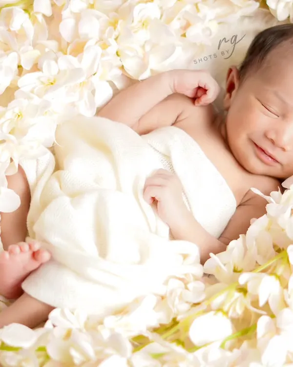 A happy little angel smiling in her sleep, surrounded by a bed of delicate white flowers. This is a perfect example of a pure and simple newborn portrait.
