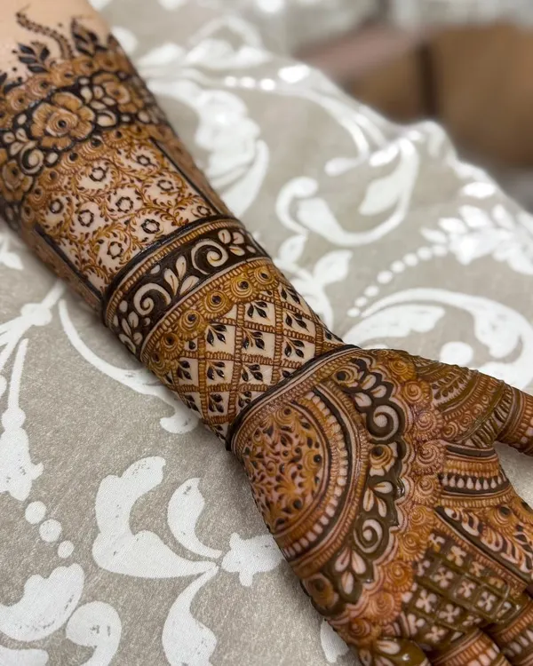 A close-up view of a highly detailed Indian henna design. This piece features a wide cuff with geometric lattice work, intricate floral bands, and delicate patterns covering the palm and fingers.