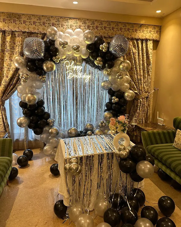A full view of our popular disco-themed birthday decor. We use a circular balloon arch in black, silver, and white, a shimmery silver curtain, and a "Happy Birthday" neon sign to create the ultimate party vibe right in your living room.