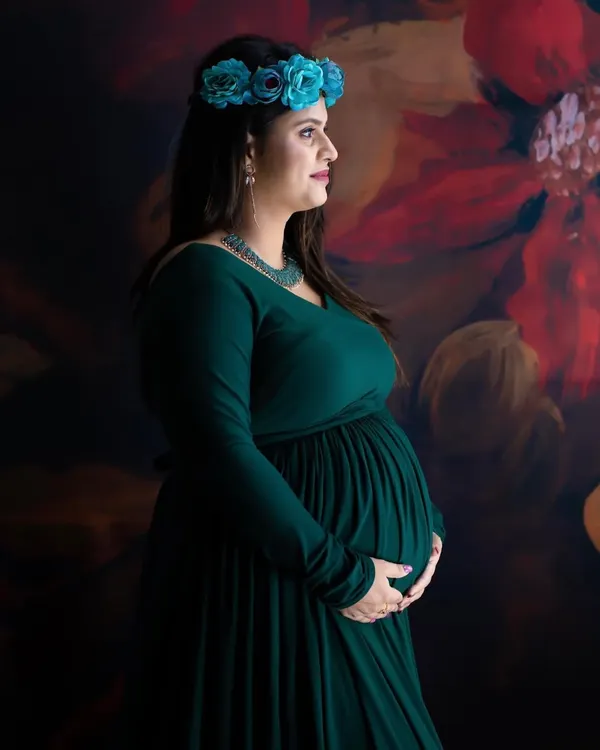 A beautiful profile shot of a mom-to-be in a dark green gown, wearing a blue floral crown. The painted backdrop adds an artistic touch to this serene portrait.