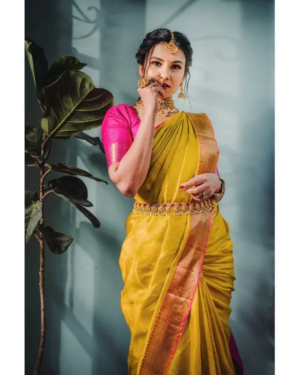 A classic portrait showcasing a vibrant yellow silk saree. The use of natural side lighting highlights the fabric's texture and the intricate details of the traditional jewelry.