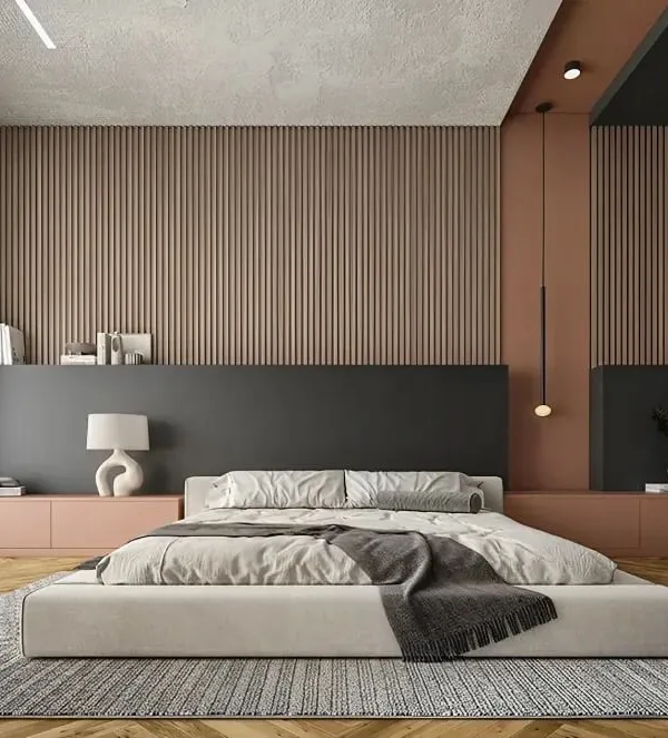 A minimalist bedroom design featuring a low-profile bed and a striking paneled accent wall. The combination of soft pink, deep charcoal, and wood textures creates a calming and contemporary atmosphere.