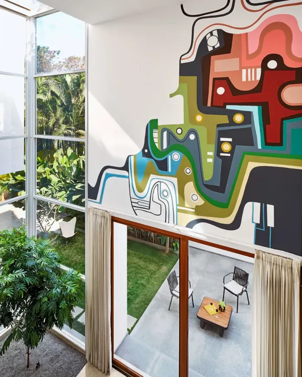 An aerial view of the Split House, highlighting the double-height living space and the vibrant custom mural. The large glass walls open up to the garden, ensuring the home is always connected to the outdoors.