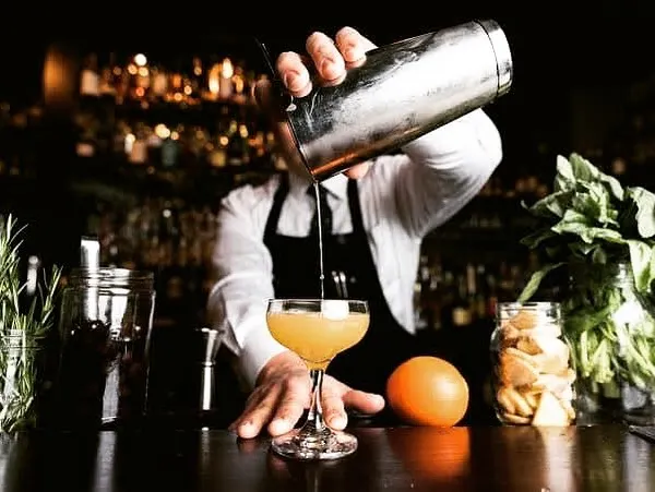 A classic cocktail being shaken and poured by a professional bartender. This shot captures the focus and expertise that goes into making a perfectly balanced drink.