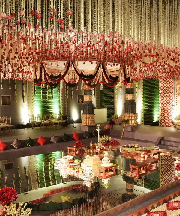 The central mandap area, set over a mirrored surface reflecting the stunning floral ceiling. Inspired by the Brihadishwara Temple, this design features tiered seating for guests, intricate floral pathways, and towering deity paintings, creating a 360-degree immersive experience.