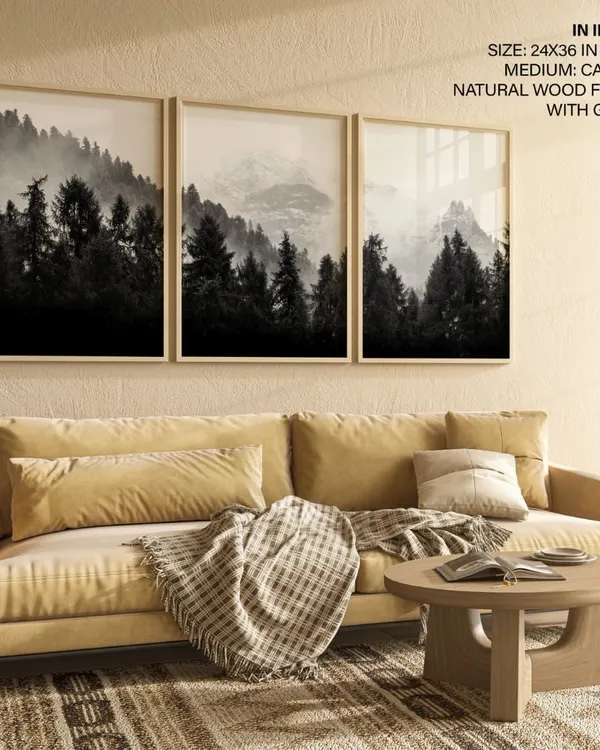 Create a dramatic and moody atmosphere with this set of three black and white forest photographs. The misty mountain scenes, framed in natural wood, work together to form a stunning panoramic landscape above a sofa.