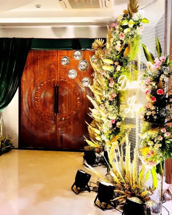 A stunning entrance to a Sangeet night, featuring a massive floral installation with a neon sign, setting a glamorous and exciting tone for the evening.
