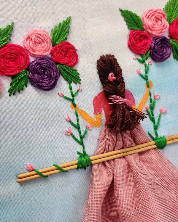 This is a mixed-media embroidery piece I created, featuring a girl on a swing. I used thread for her hair and the flowers, and a piece of fabric for her dress to give it a 3D effect.