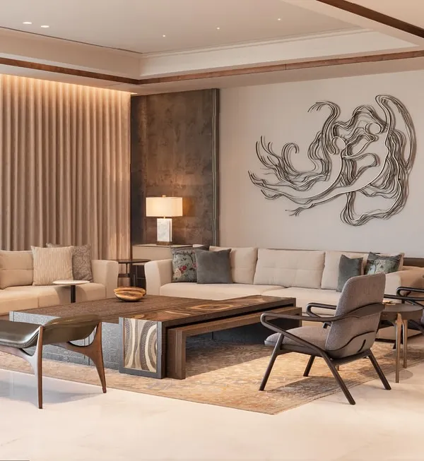 A living room at DLF Camellias where contemporary design meets Indian elements. The neutral sofa is accented with colorful cushions, while the back paneling highlights a stunning metal artwork, creating a space that is both modern and rooted.